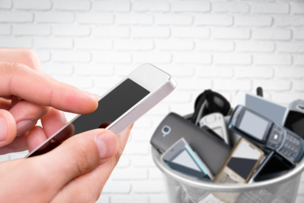 Hand with phone and rubbish bin full of old cellphones